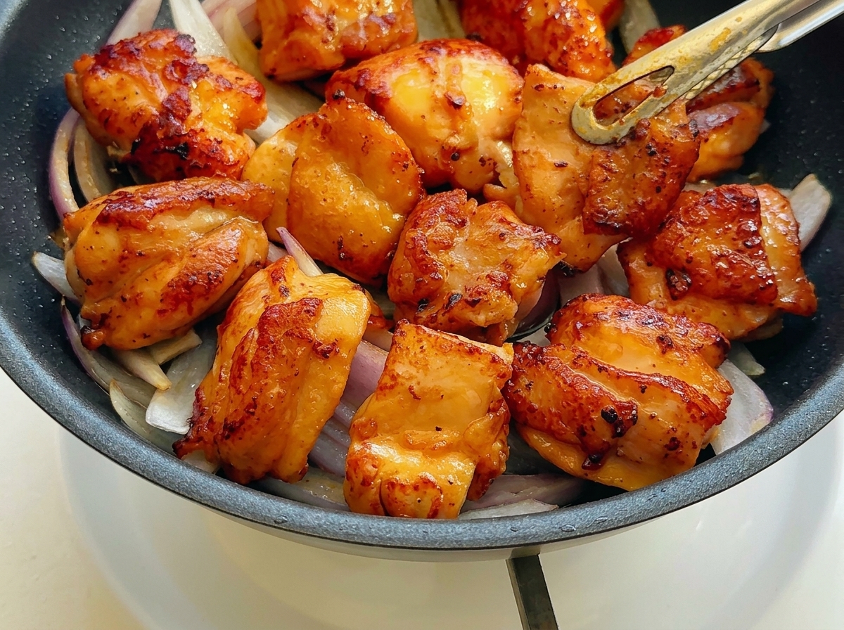 Golden brown pan-fried chicken pieces arranged neatly on top of sautéed sliced red onions in a black skillet.