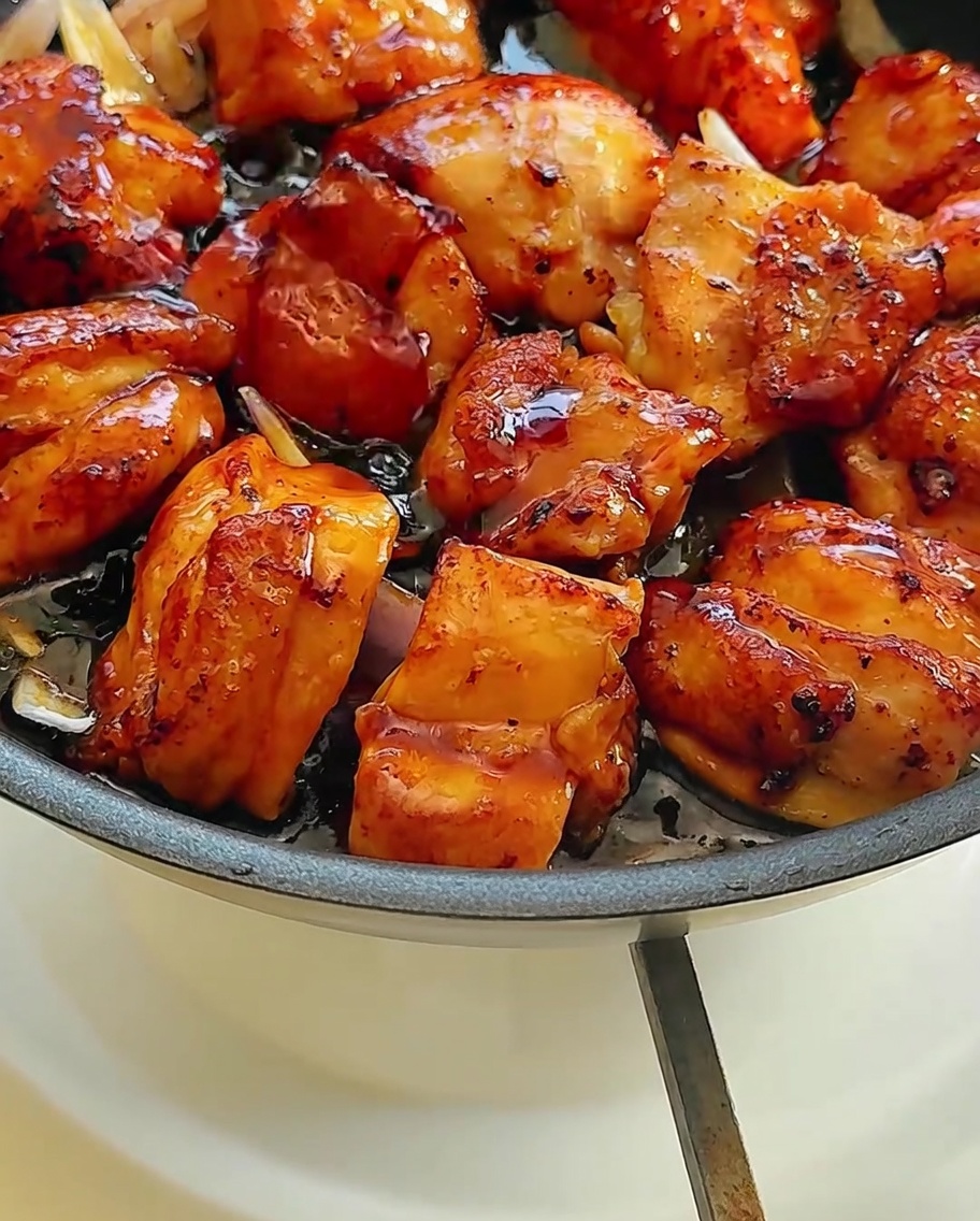 The chicken and onion mixture in the pan being coated with a dark, savory soy-based sauce.