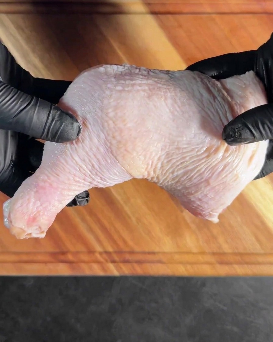 A deboned chicken thigh lying flat on a wooden cutting board.