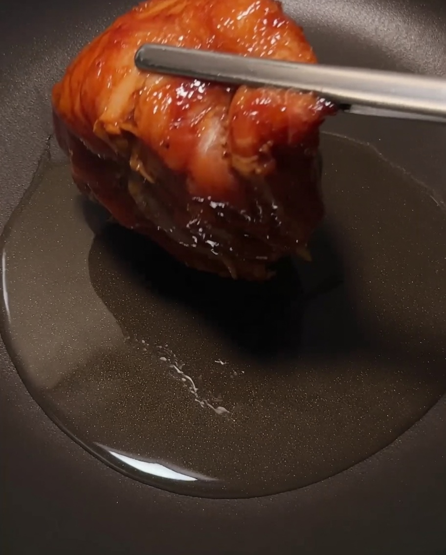 The chicken thigh frying in a skillet, focusing on the crispy skin.