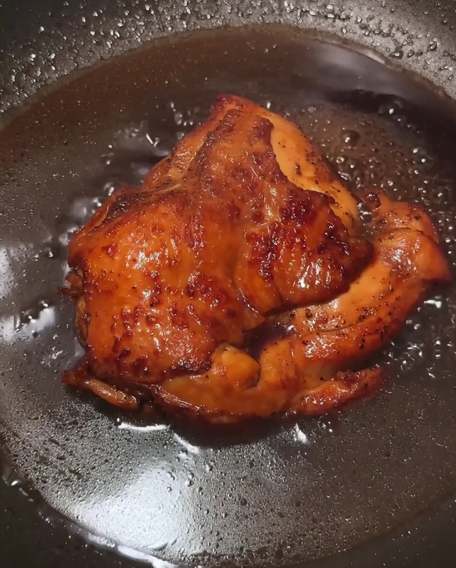 A dark, savory sauce bubbling in a pan with chicken pieces, becoming thick and glossy after the addition of cornstarch slurry.