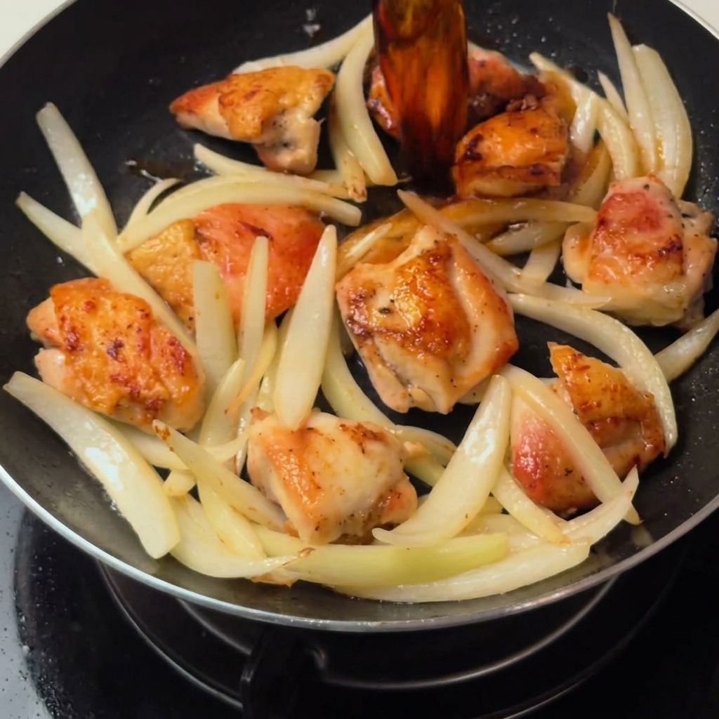The chicken and sautéed onions simmering in the savory dashi-based sauce inside the pan.