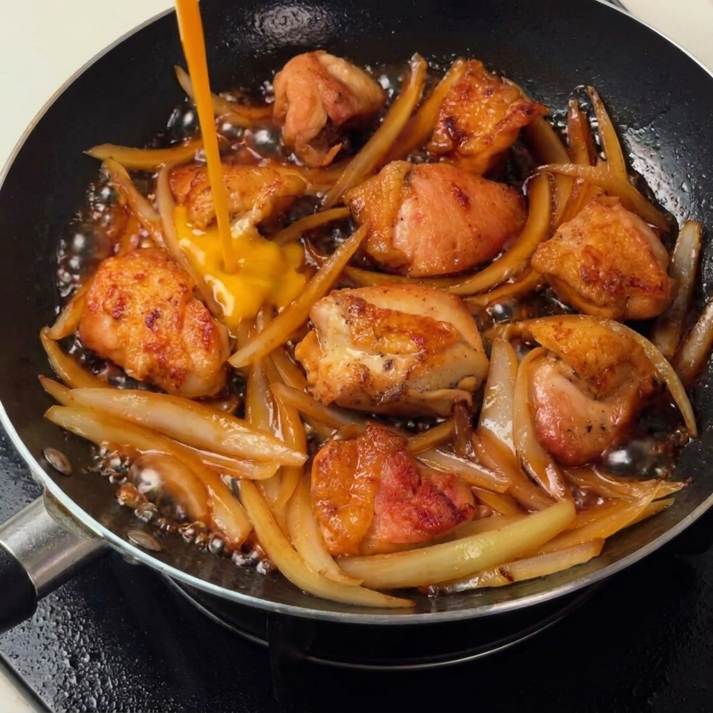 Whisked eggs being poured into the pan over the chicken and onion mixture, creating a light coating.