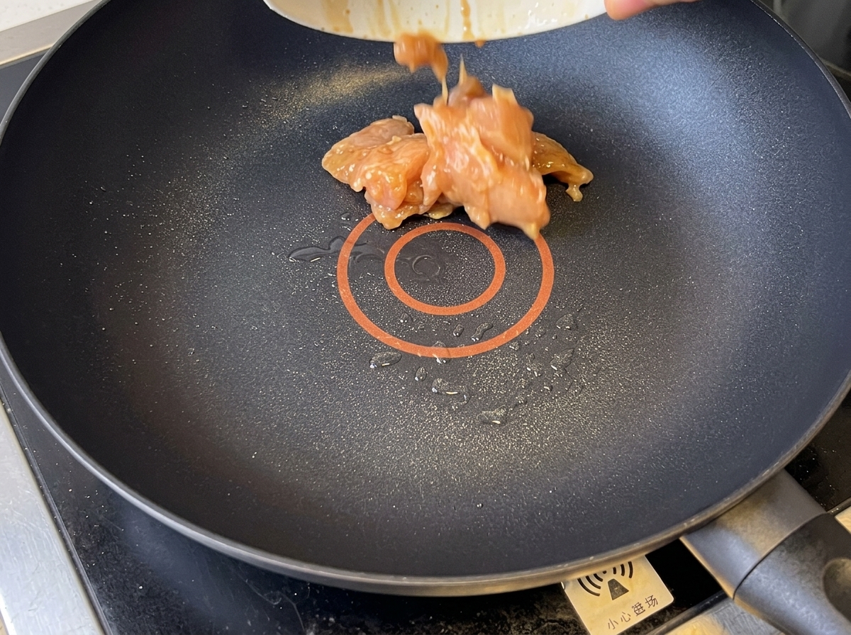 Golden-brown chicken pieces being stir-fried in a non-stick pan.