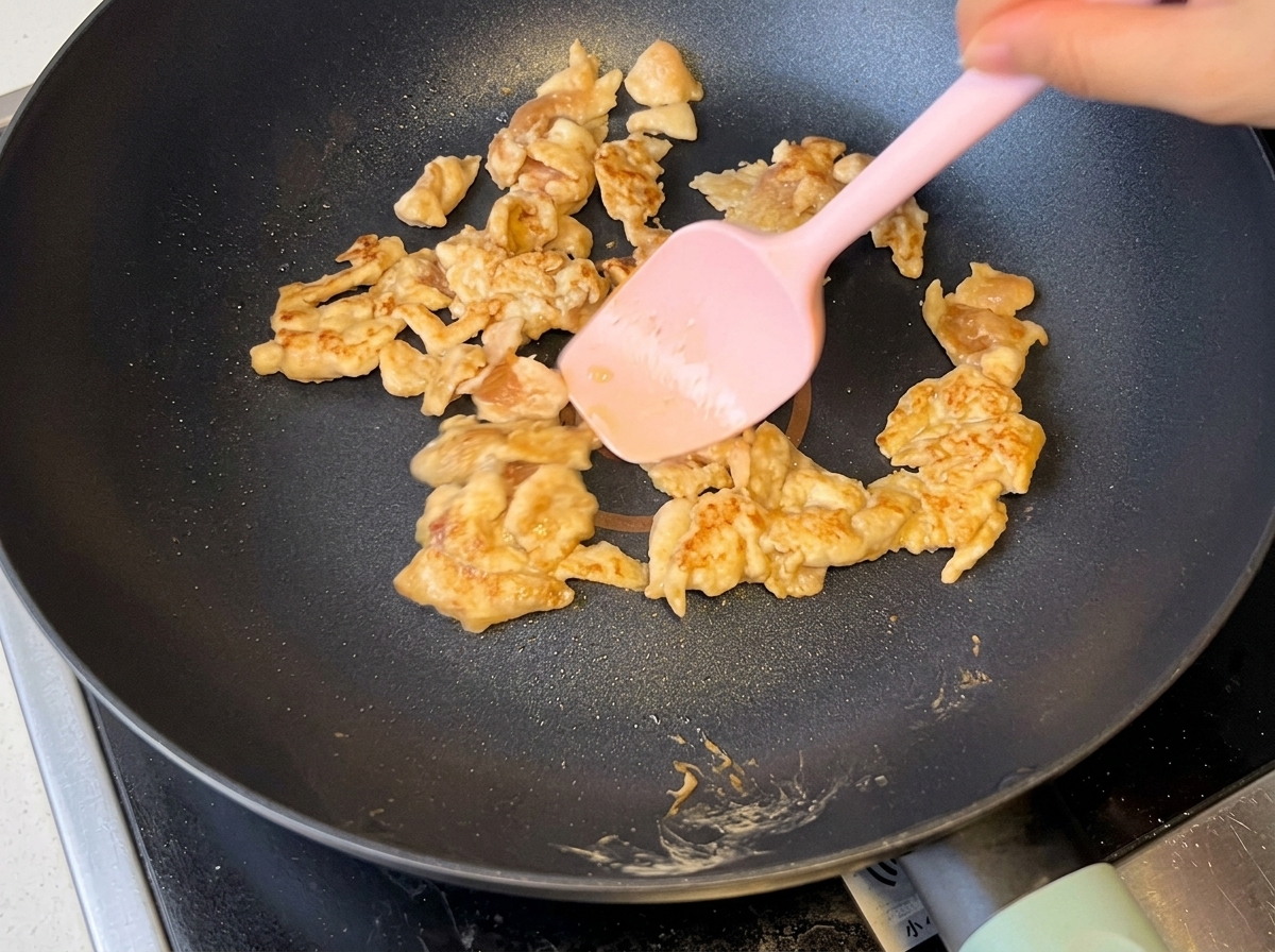 Sliced onions being stir-fried alongside browned chicken in the pan.