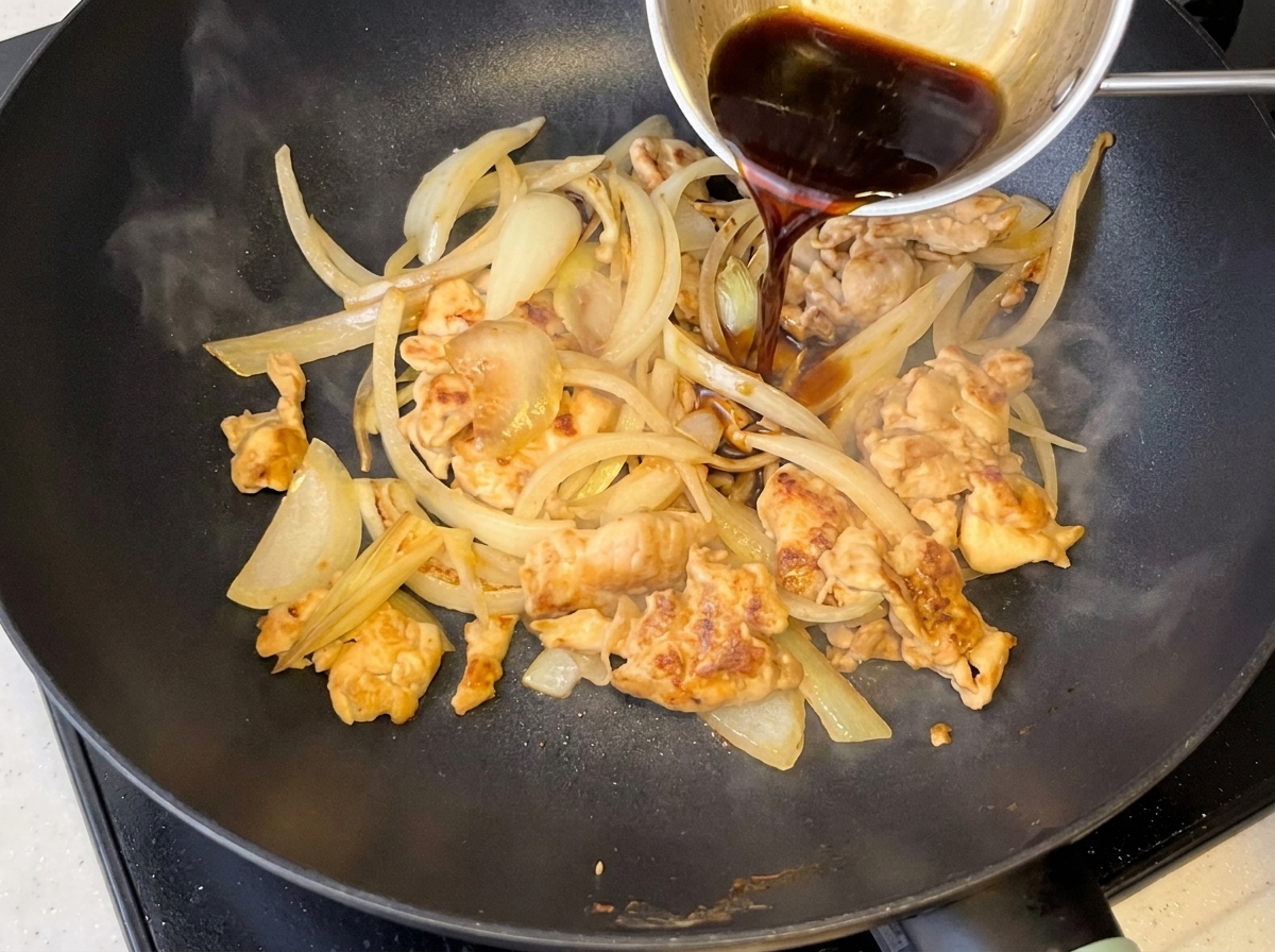 Dark sauce being poured into a pan containing chicken and softened onions.