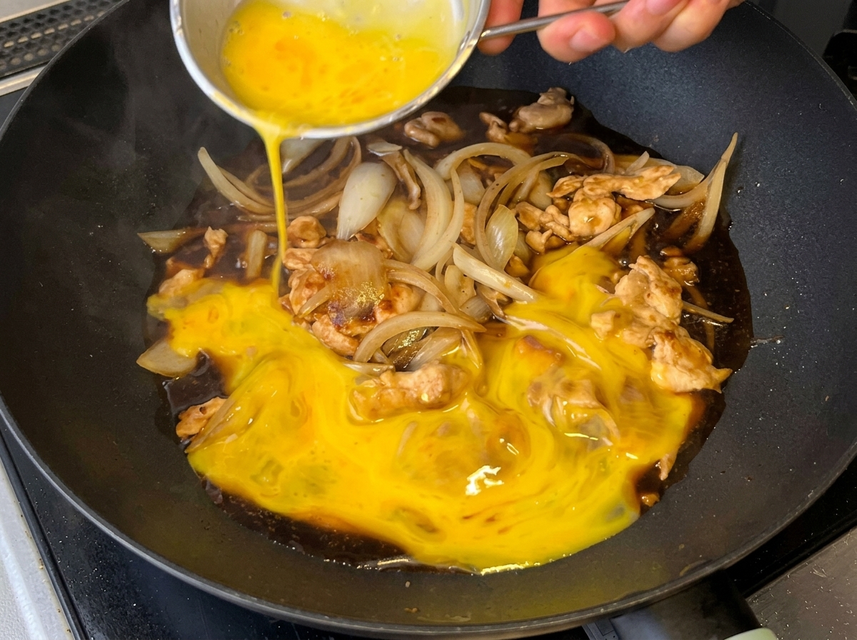 Beaten eggs poured over the chicken, onion, and sauce mixture in the pan.