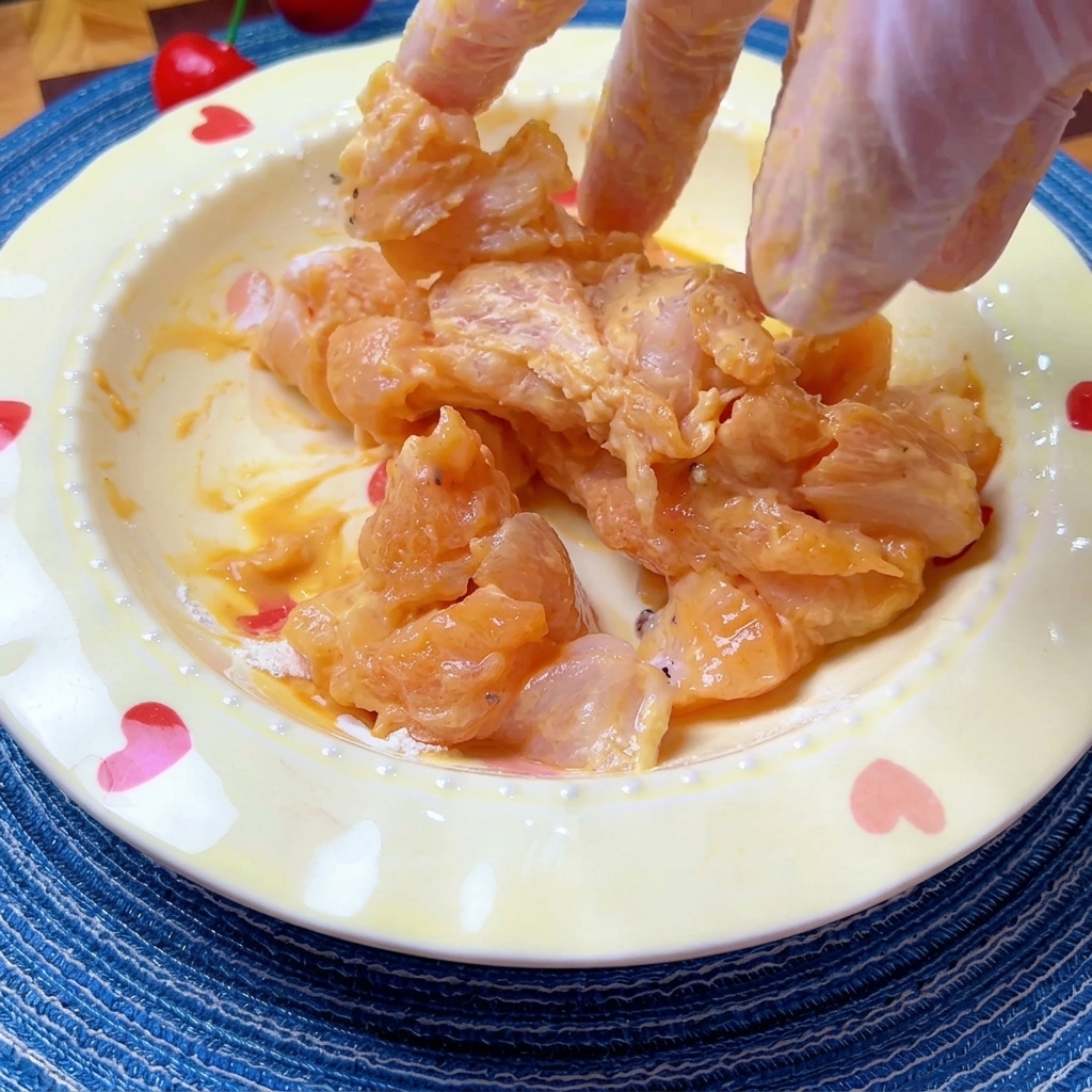 Marinated chicken pieces being mixed by hand in a bowl to ensure even coating.