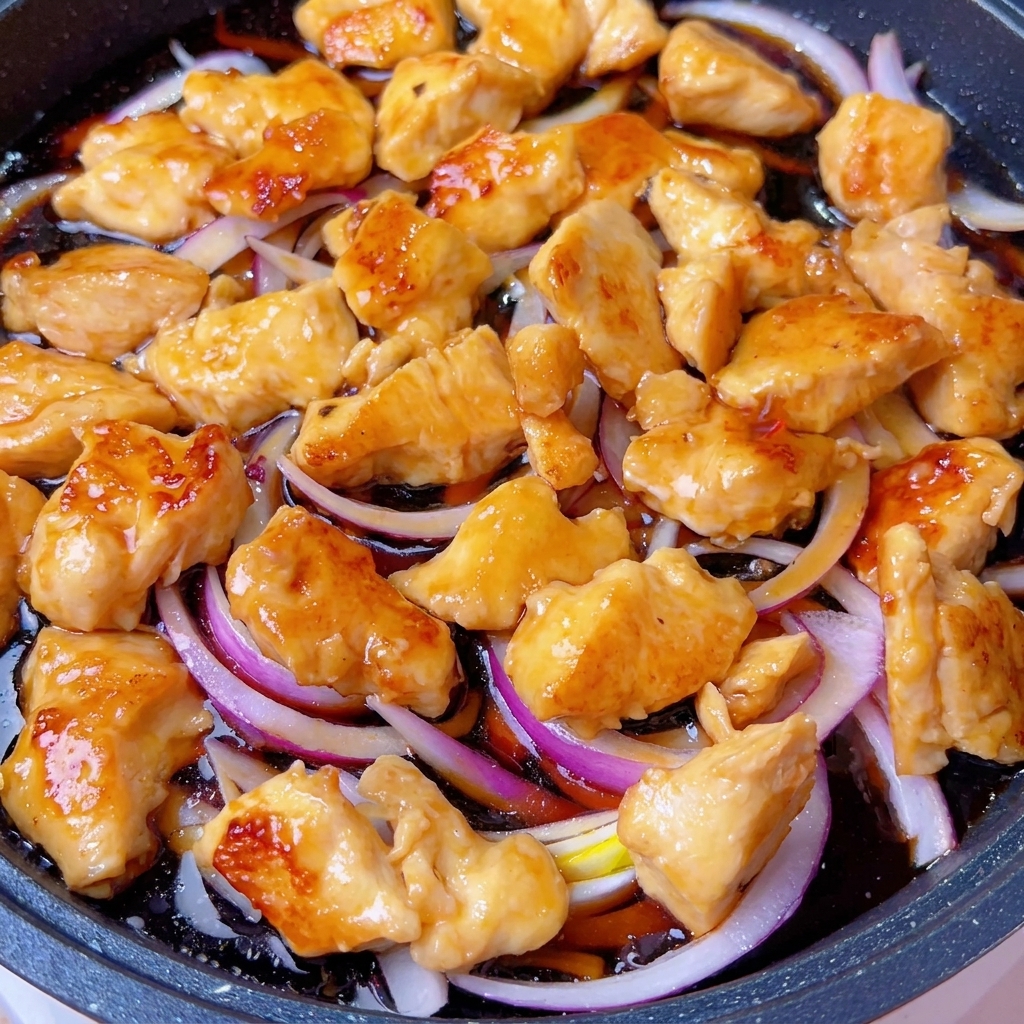 A covered pan on the stove, with the chicken and onion mixture simmering inside.