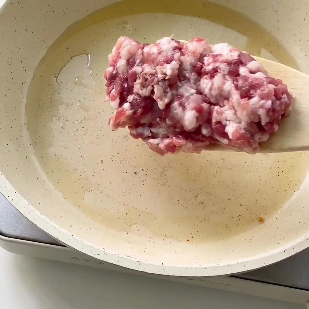 A close-up of fresh minced meat being added to a pan with hot oil.