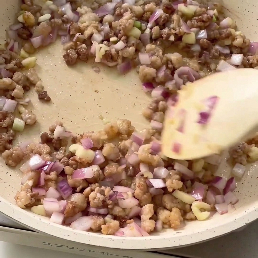 Seasoning ingredients being added to the pan with minced meat and onion.