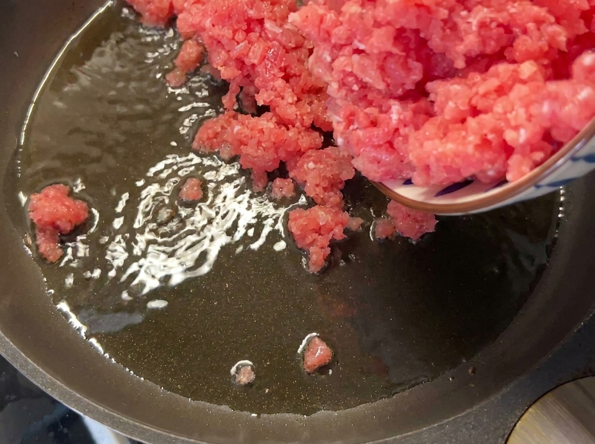 Ground lean pork being added to a hot, oiled pan.