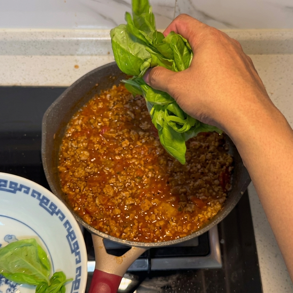 Fresh basil leaves being added to the finished meat and tomato sauce.