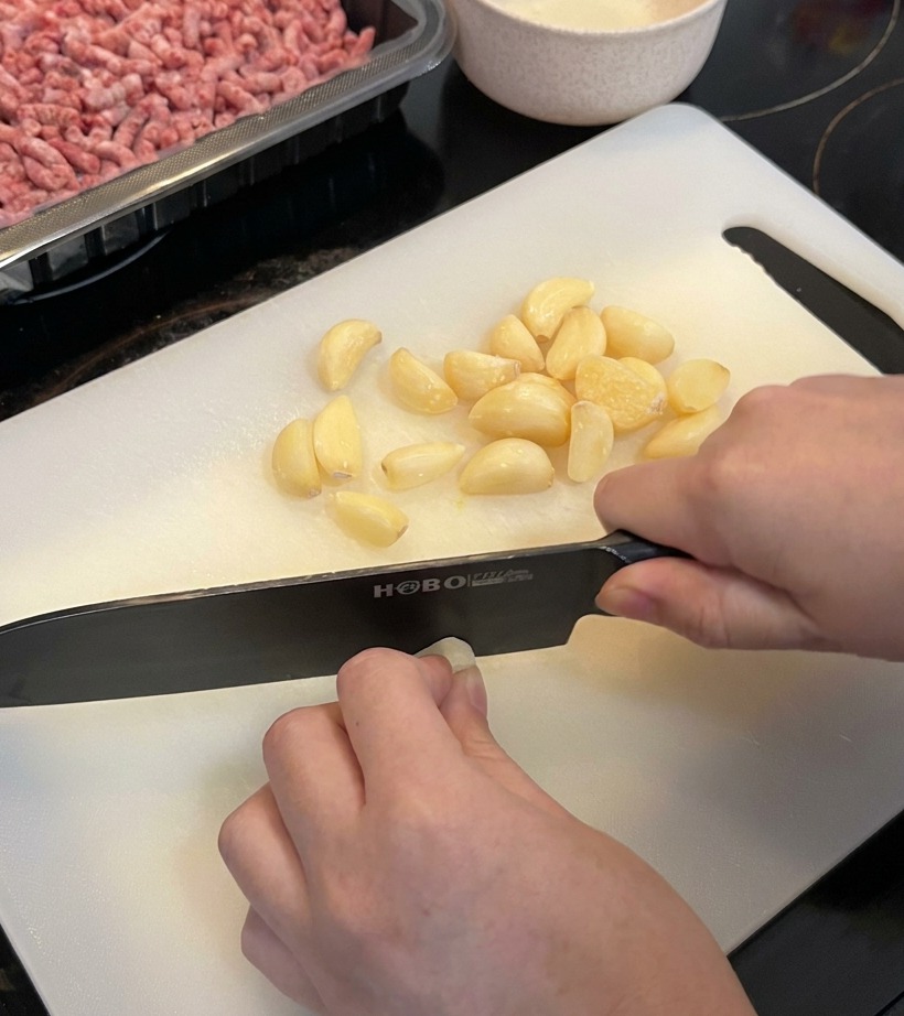 A close-up view of a large mound of fresh garlic cloves being chopped on a clean white cutting board.