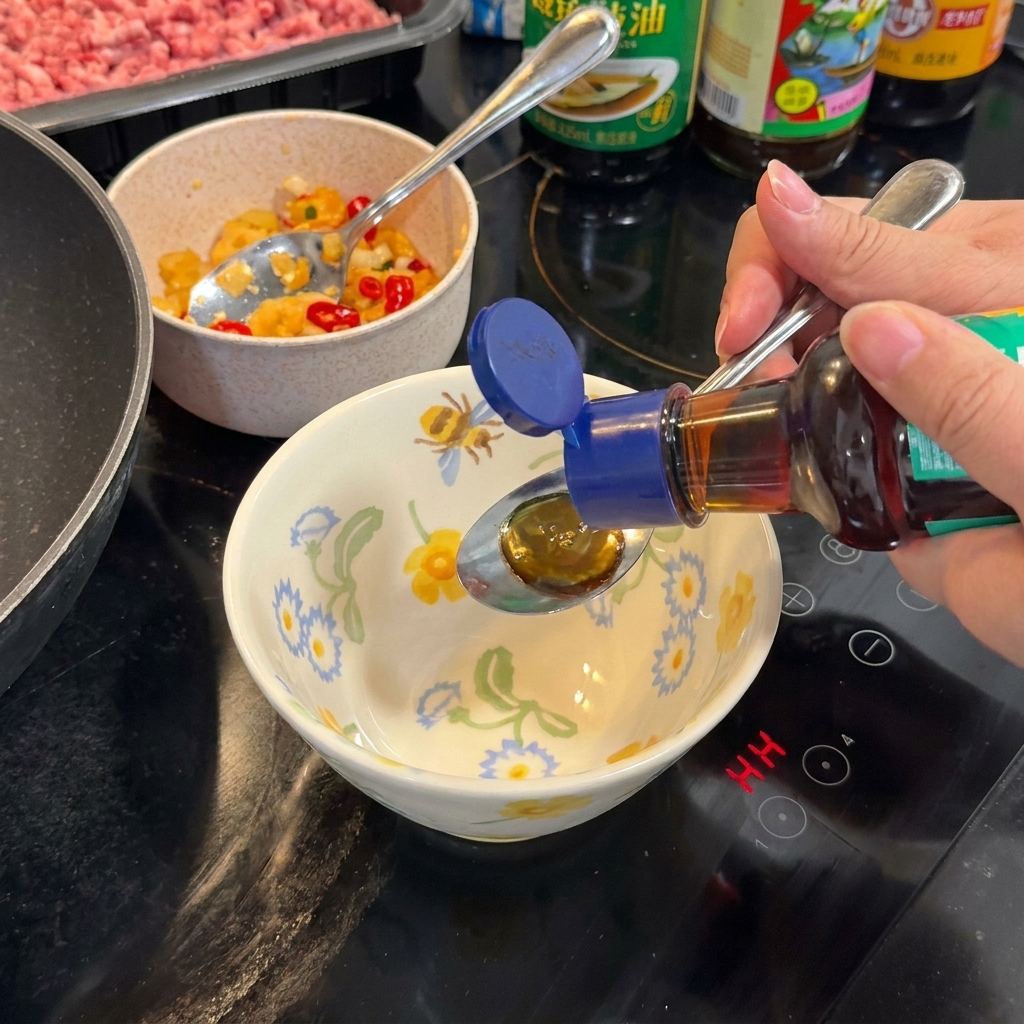 A spoon stirring a dark, savory sauce mixture in a floral-patterned bowl on a stovetop.