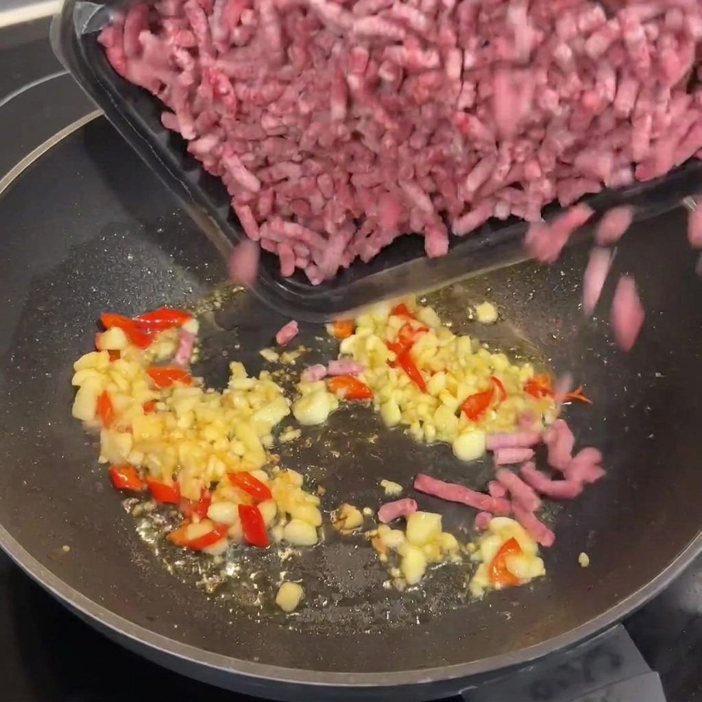 Raw Wagyu beef mince being added to the hot wok with the sautéed garlic and chilies.