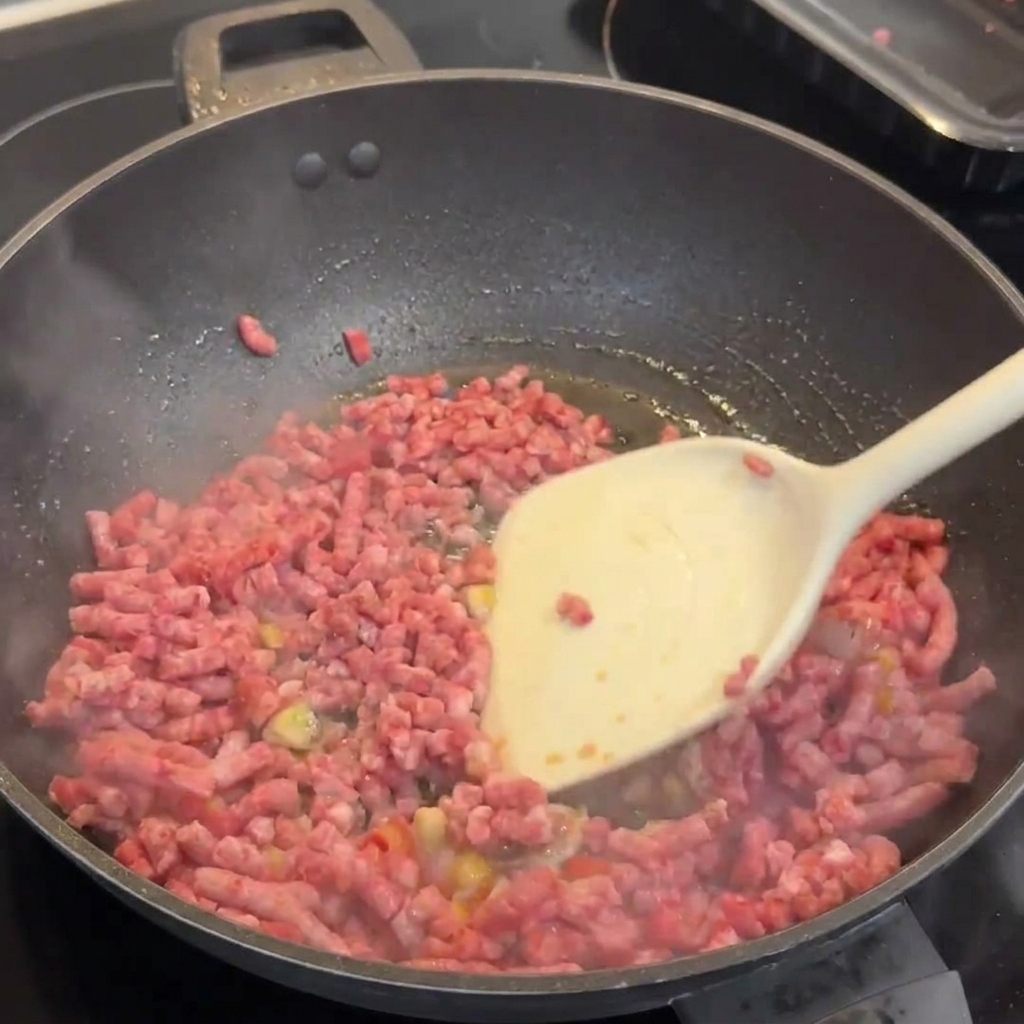 Wagyu beef mince browning in a wok with garlic and chilies, being broken apart with a white spatula.