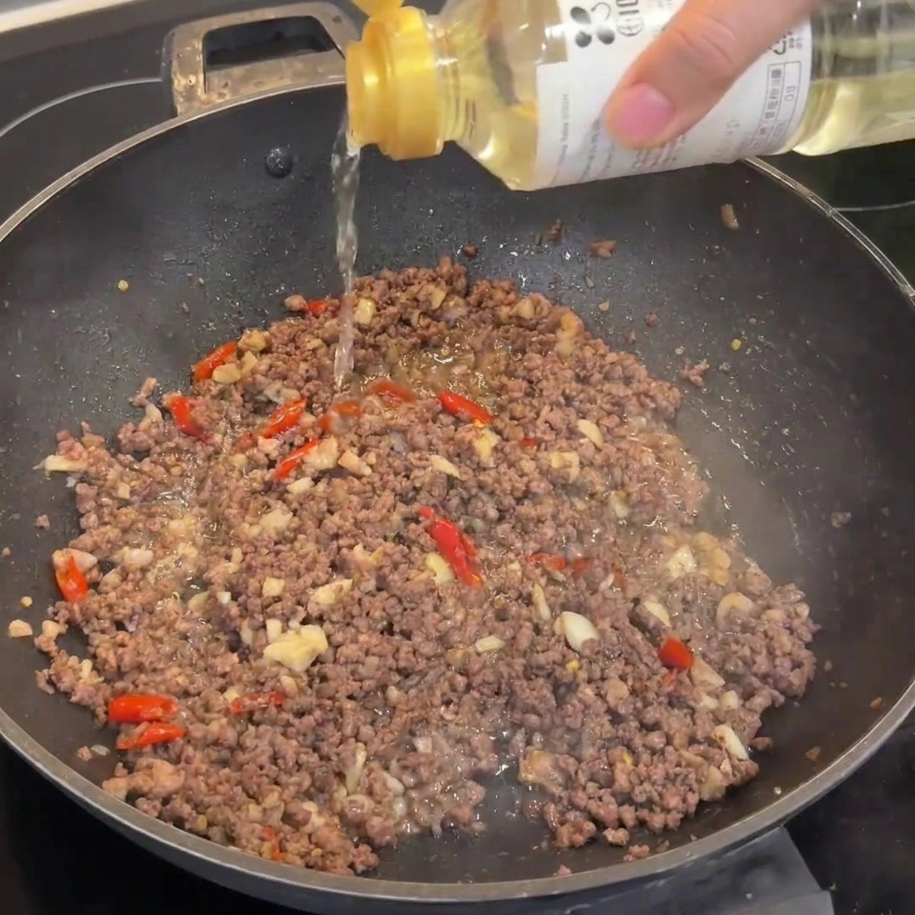 A splash of rice wine being poured into a wok containing browned beef mince.