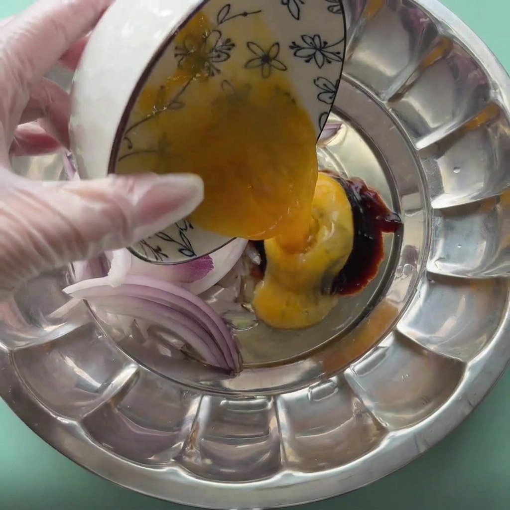 An egg being cracked into a metal bowl with sliced red onions and sauces.