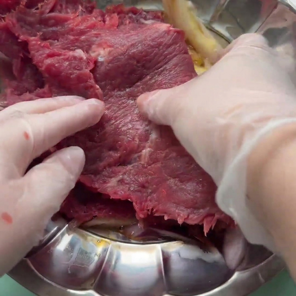 A raw beef slice being mixed into a marinade of egg, onion, and sauces in a bowl.