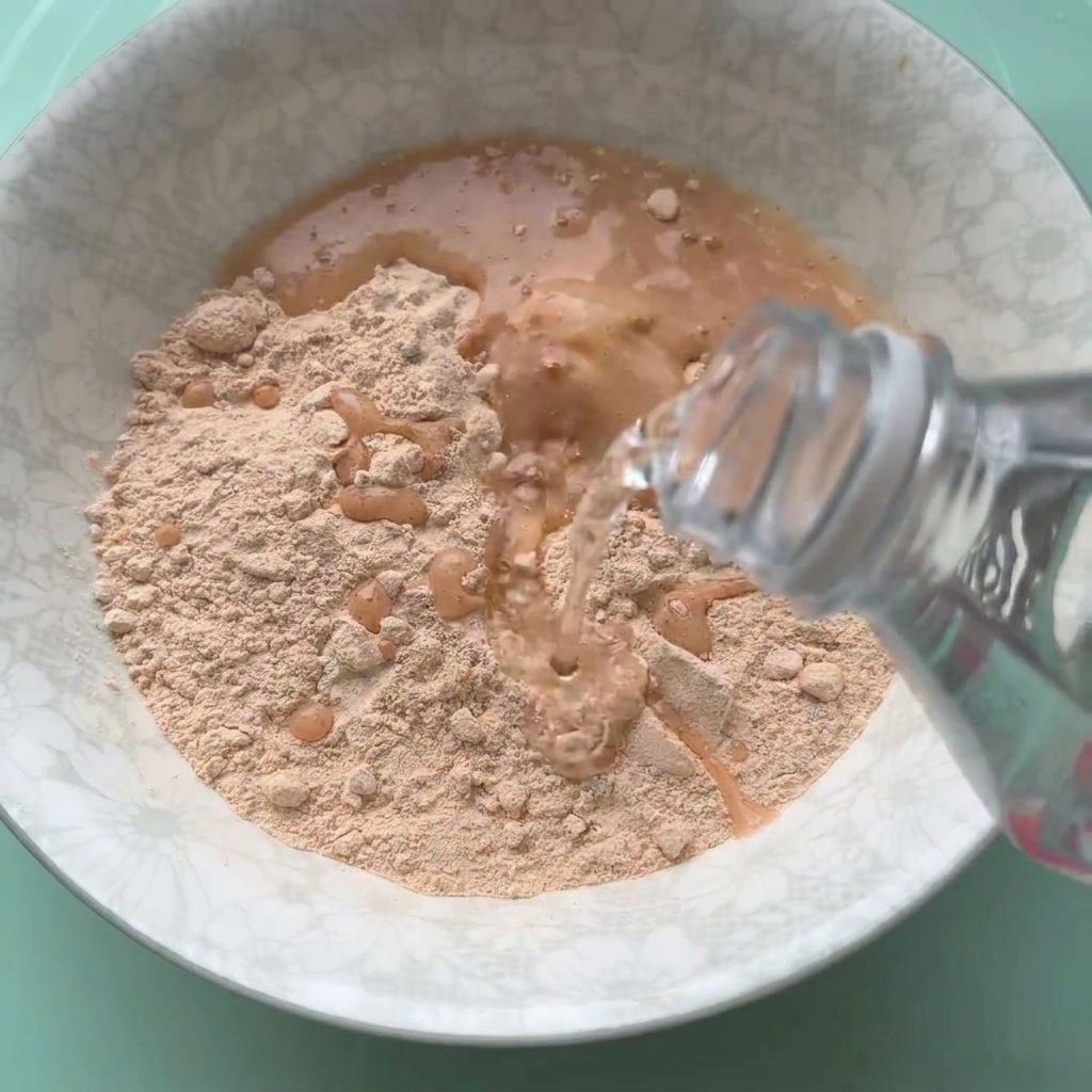 Fried chicken powder being mixed with water in a white bowl.