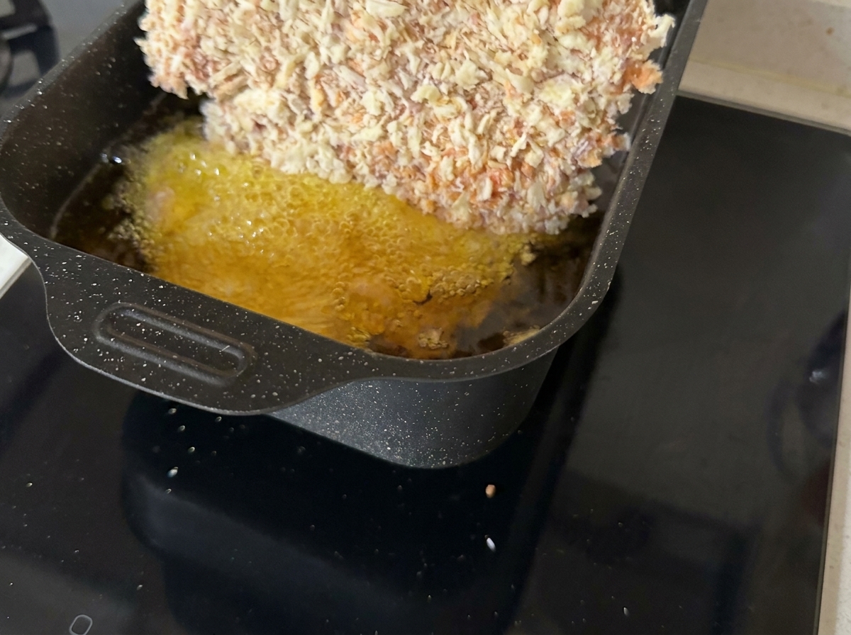 A breaded beef cutlet frying in a shallow pan of hot, bubbling oil.