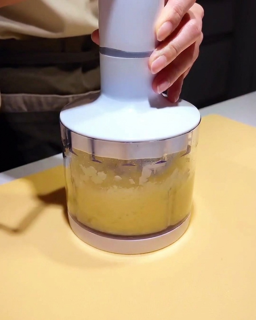 A small blender cup filled with a light yellow puree and dark marinade, ready to be blended.