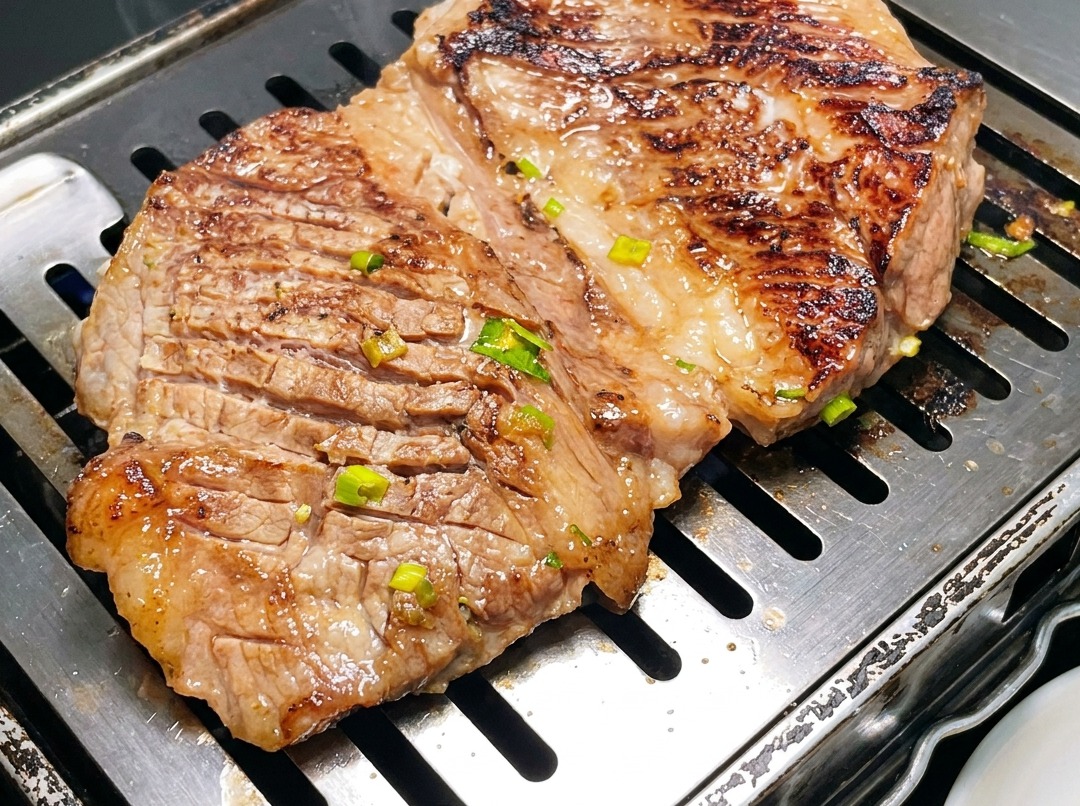 A close-up of Korean-style beef short ribs being cut into smaller sections with scissors on a hot grill pan.