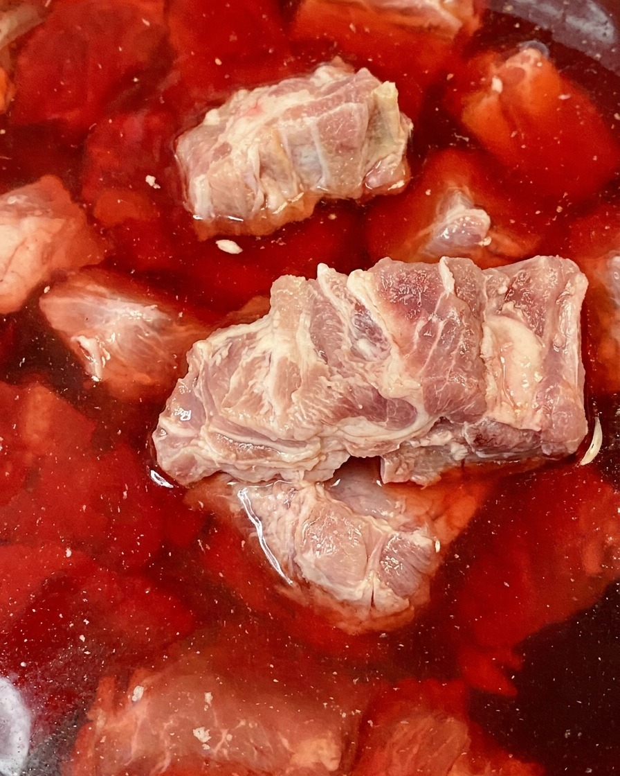 Raw pork spine bones submerged in a bowl of red, blood-tinged water.