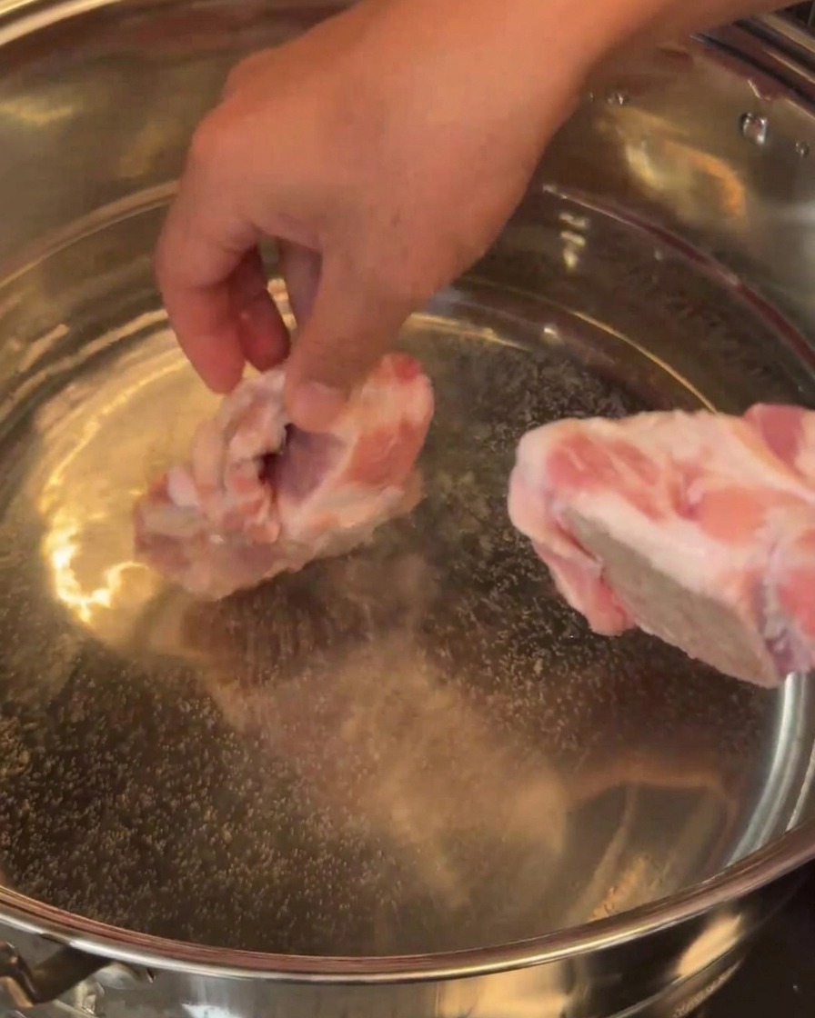 Raw pork bones being carefully added to a large pot of water.