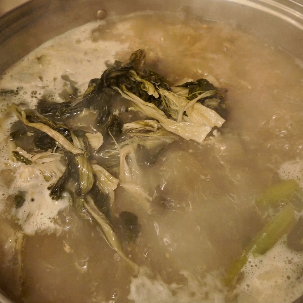 Minced garlic being scraped from a small white bowl into the bubbling stew.