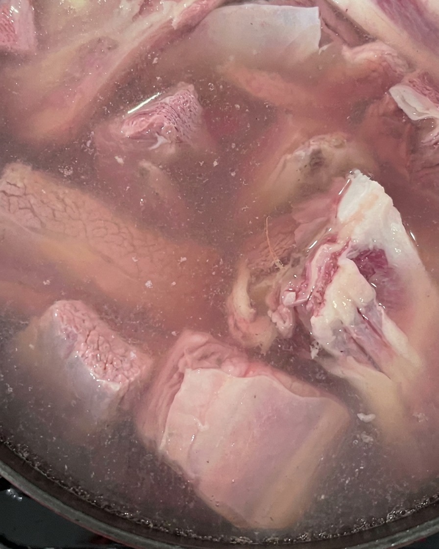 Raw beef short ribs and ginger boiling in a pot of water.