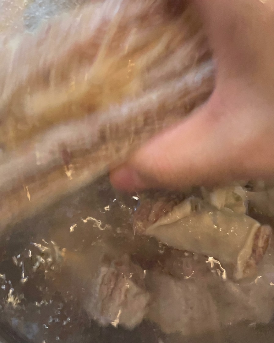 Short ribs being rinsed under running tap water, looking clean and ready for the pot.