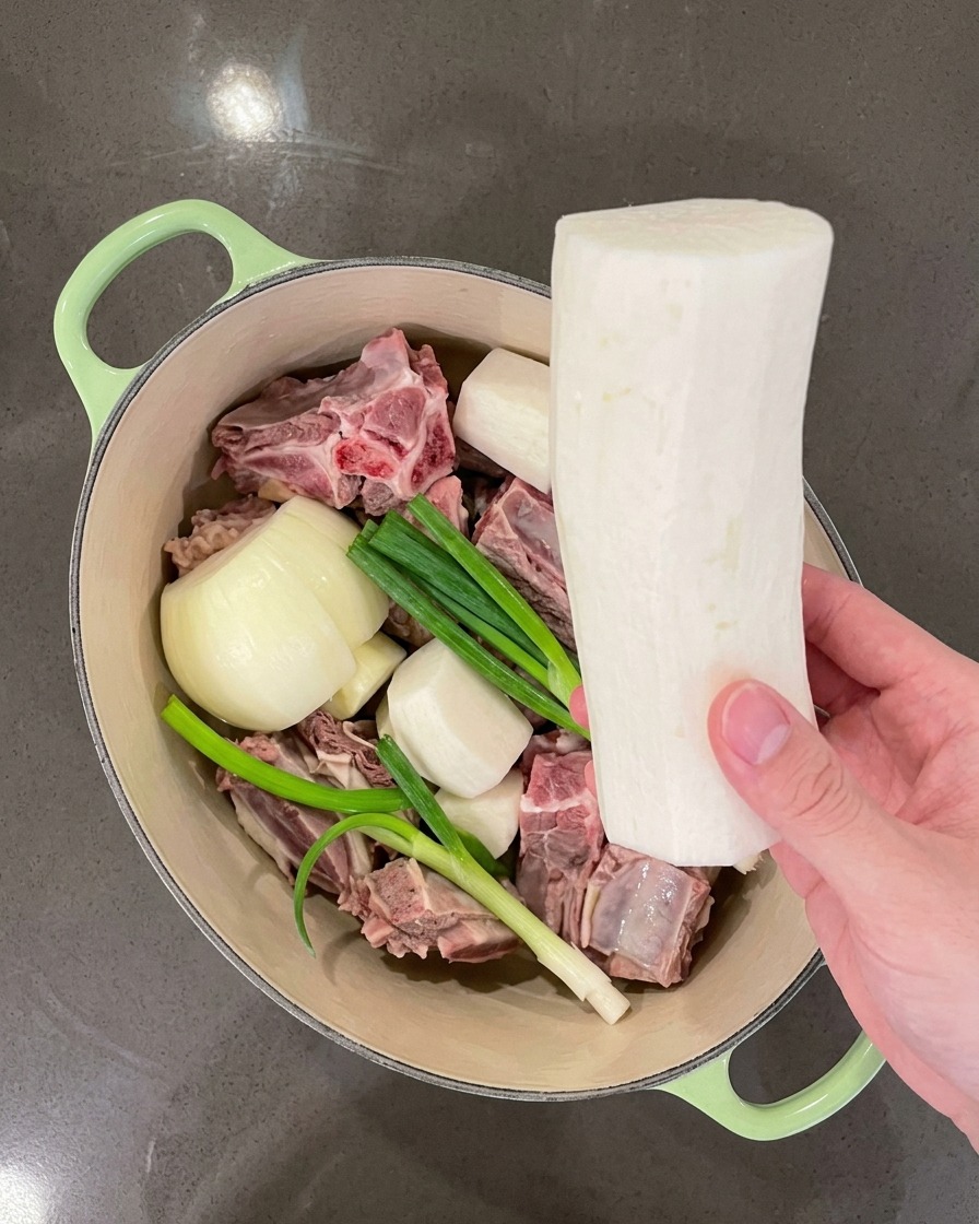 Hand placing large pieces of white radish into the pot alongside the meat and aromatics.
