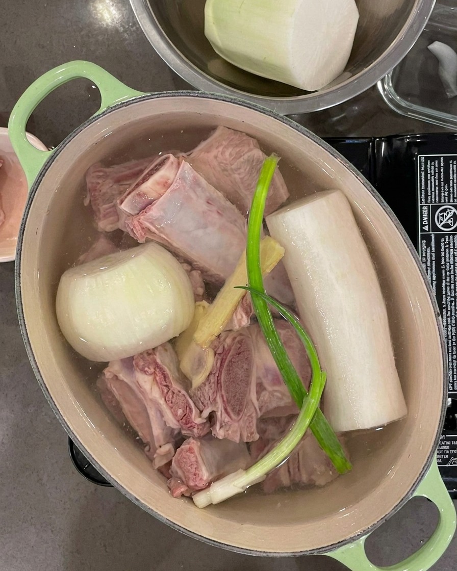 Water being poured into the pot, covering the ribs, vegetables, and aromatic ingredients completely.