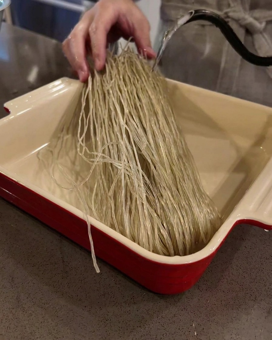Dry sweet potato glass noodles soaking in a baking dish filled with warm water.