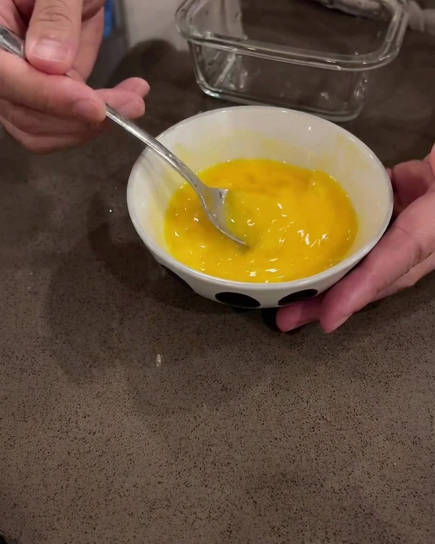 Raw eggs being whisked in a white bowl with a metal spoon.