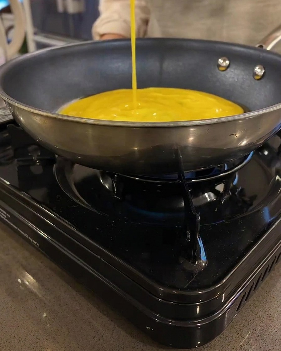 A thin yellow egg crepe cooking in a flat frying pan on a portable stove.