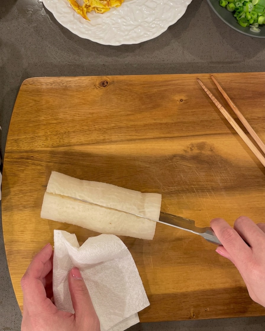 Cooked white radish being sliced into small rectangles on a wooden board.