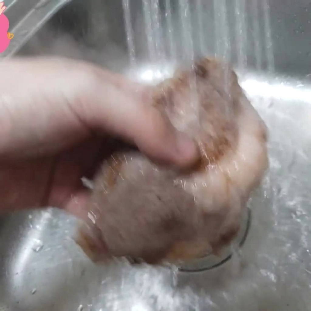 A piece of blanched beef rib being held under running water in a sink.