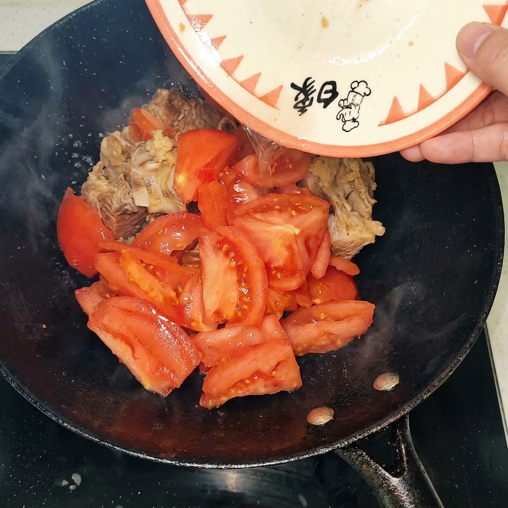 Peeled tomato chunks being added to the wok with the seared beef ribs.