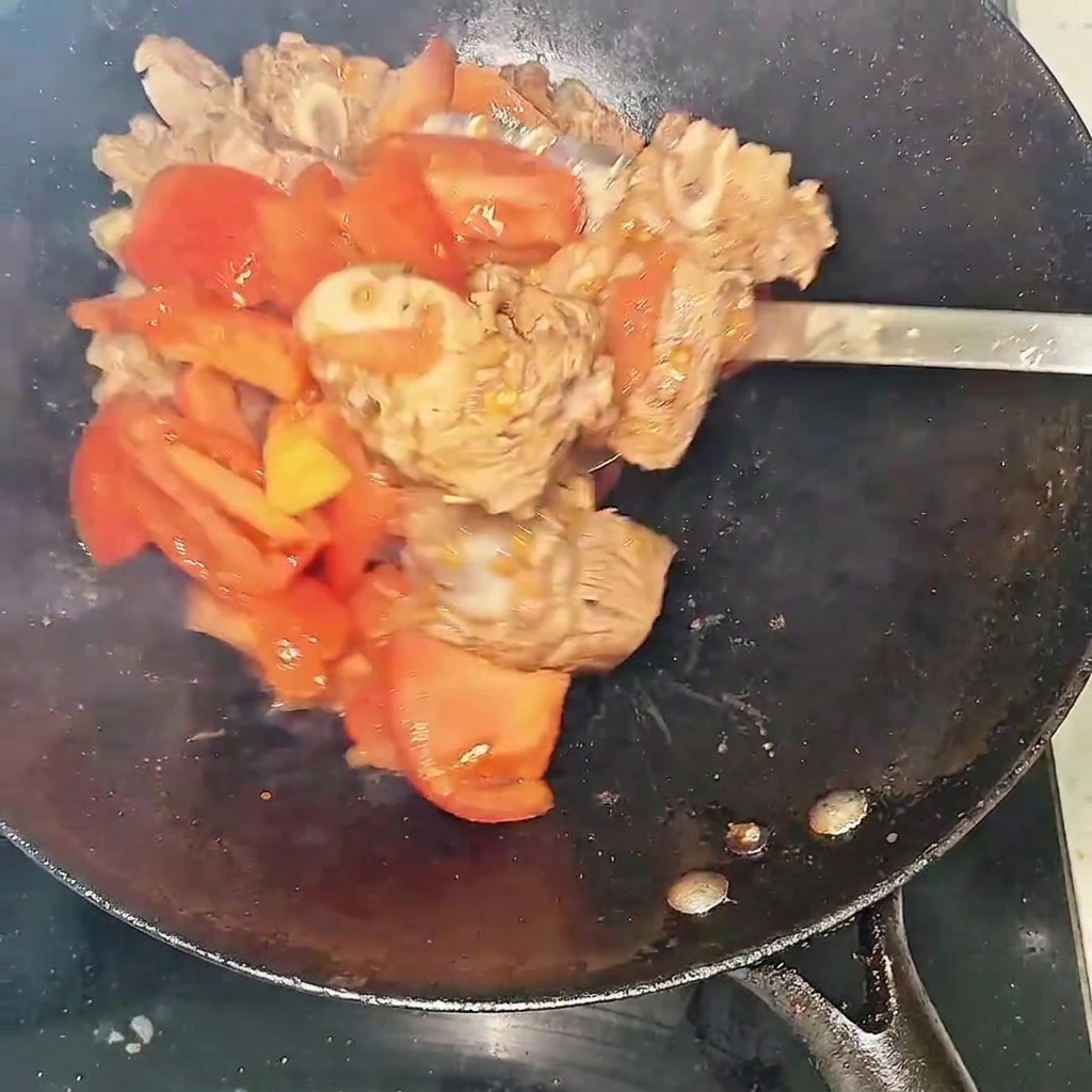 A close-up of beef ribs and tomatoes stir-frying in the wok, showing the liquid starting to form.