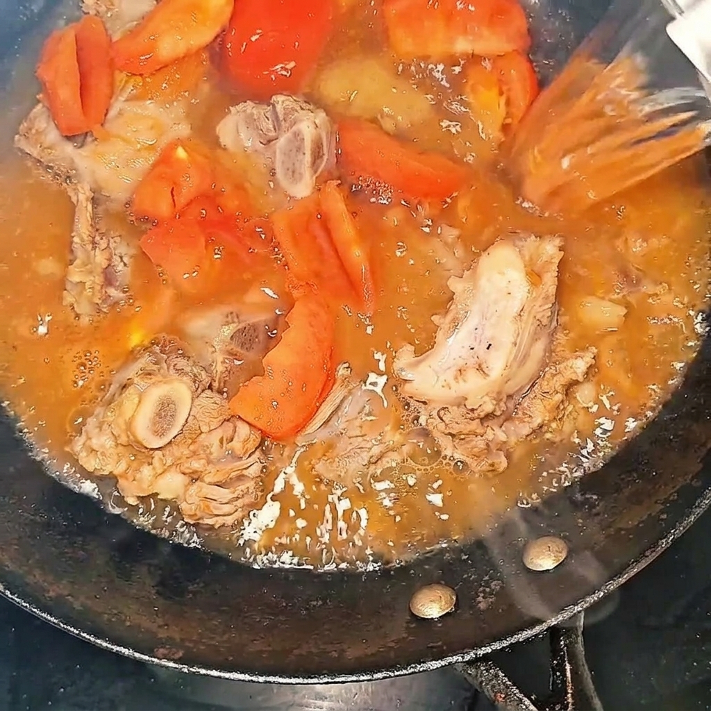 Hot water being poured into the wok with the beef ribs and tomatoes.
