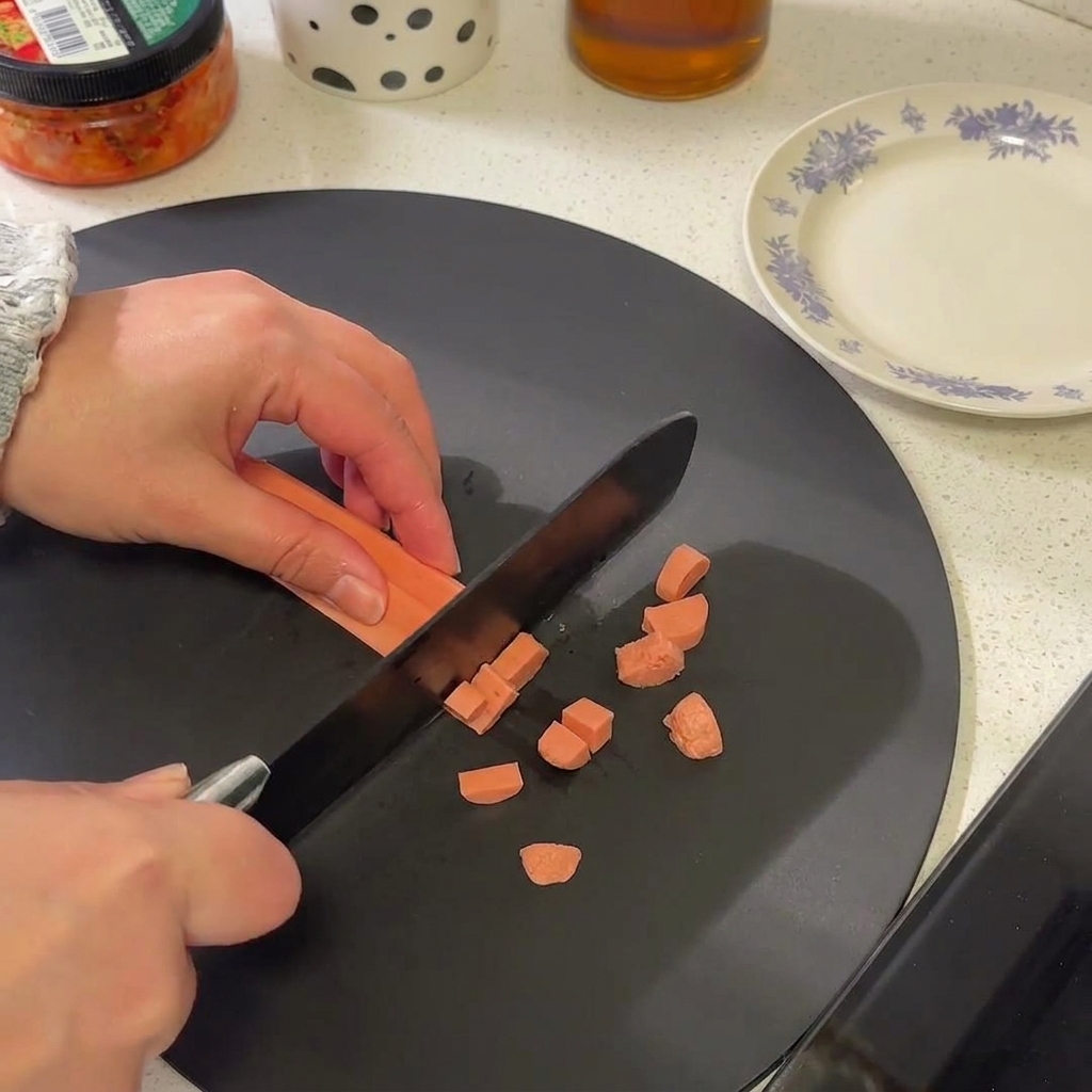 A close-up of a sausage link being sliced into small, circular rounds on a black cutting surface.