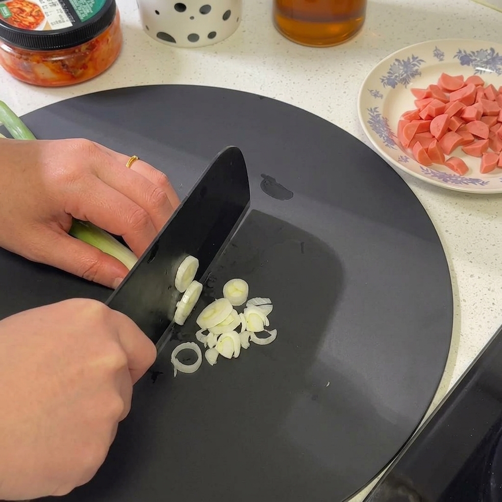 A bunch of green onions being finely sliced on a cutting board, focusing on the white and light green sections.