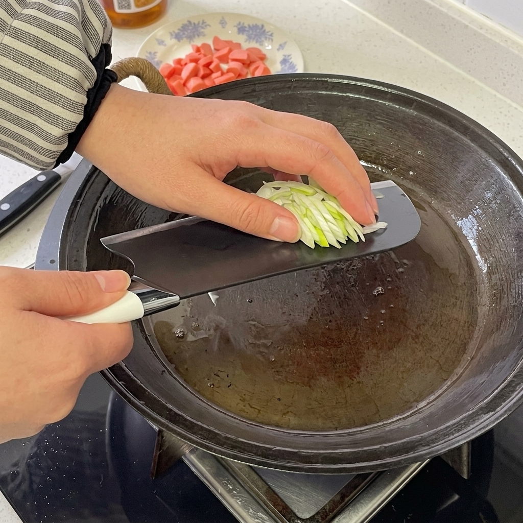 Sausage rounds and chopped green onions sizzling and being stirred together in a hot frying pan.