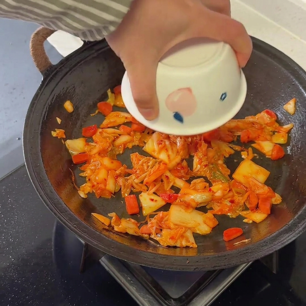 Leftover cooked rice being mixed thoroughly into the kimchi and sausage base in a hot pan.