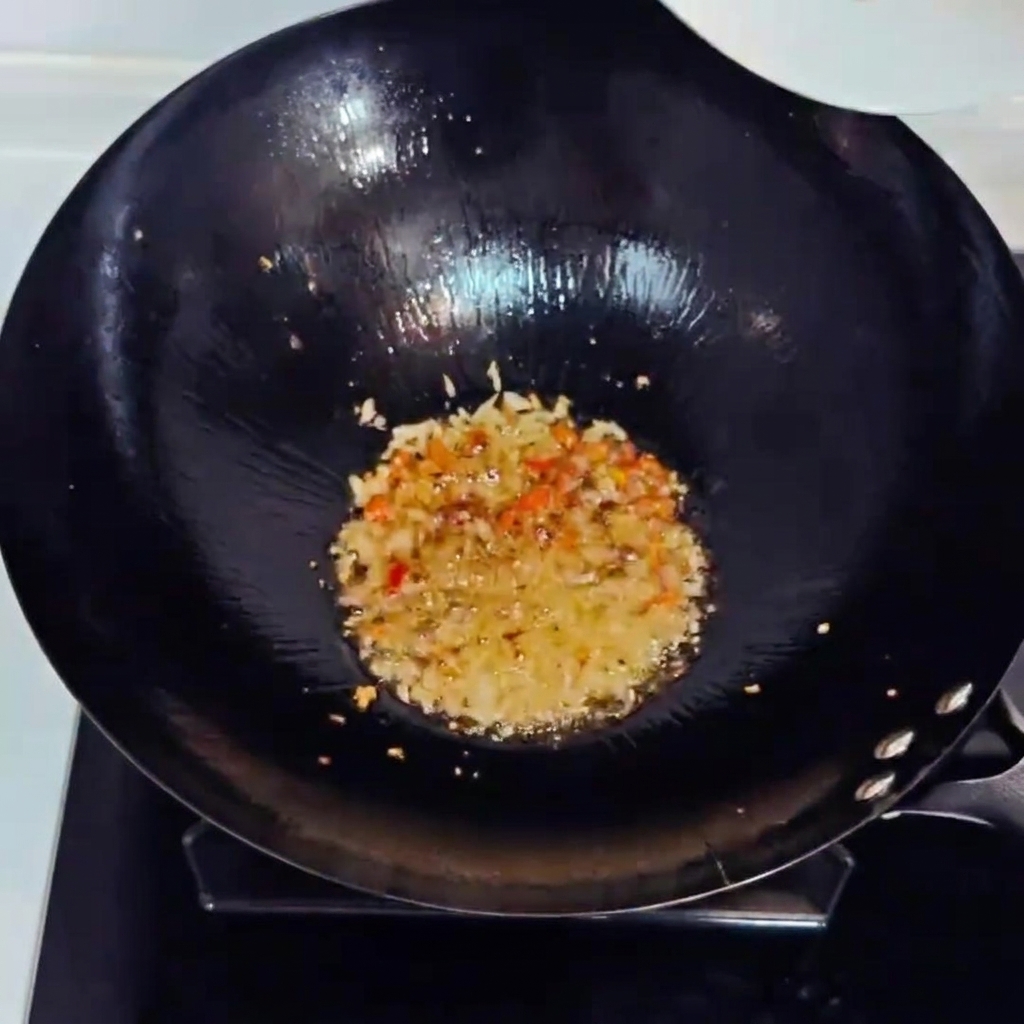 Chopped kimchi and diced ham being stir-fried in a wok with aromatics.