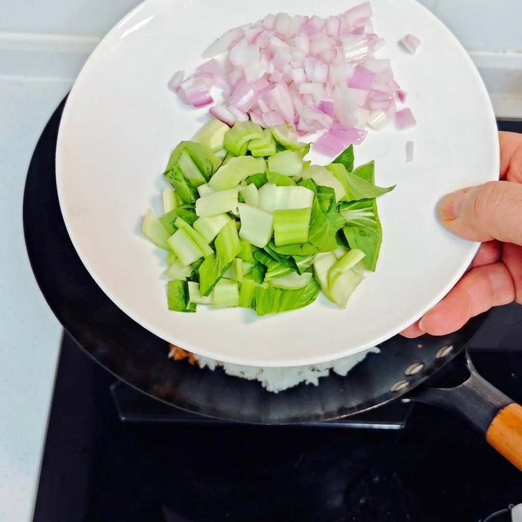 Pouring diced purple onions and chopped bok choy from a white plate into the wok with fried rice.