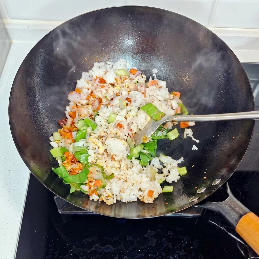 Rice, onions, and bok choy being tossed and stir-fried in a wok.